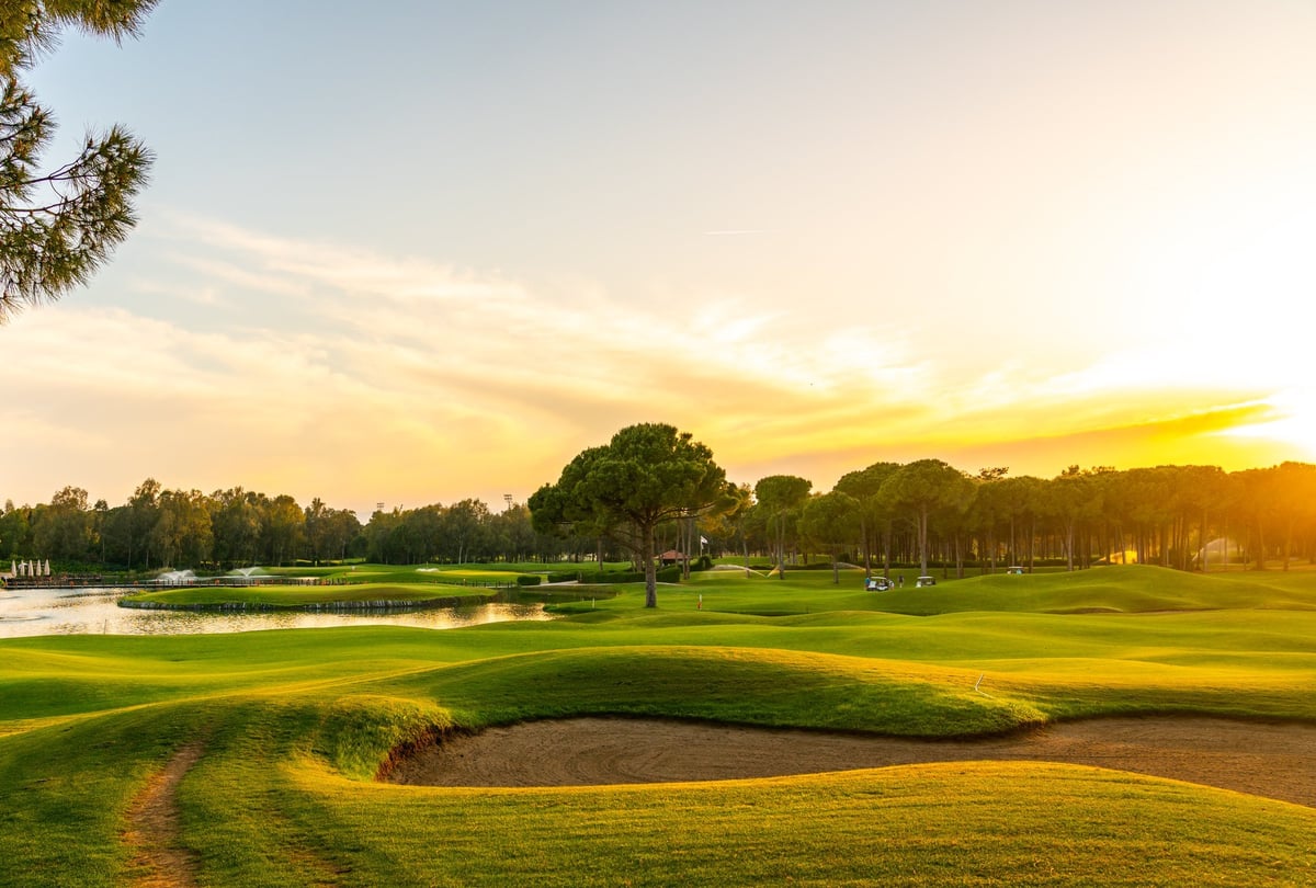 Panorama of a beautiful golf course with sand bunker, green fairways and trees at sunset