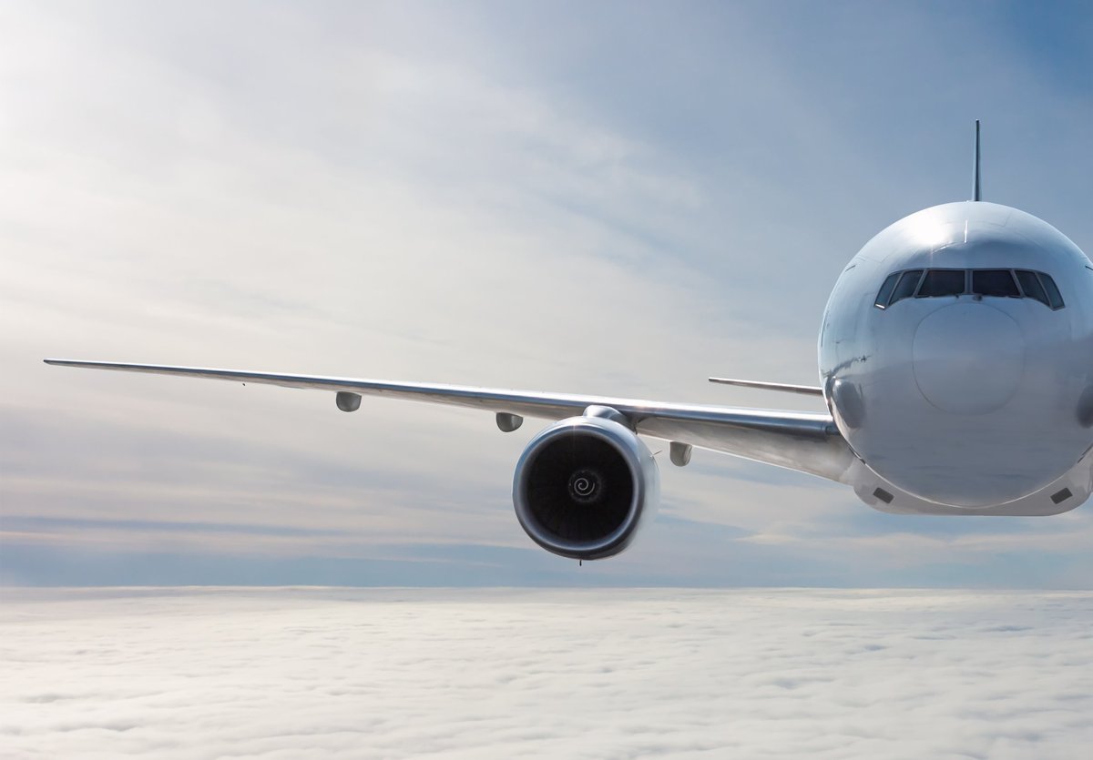 Front view of a white wide body passenger aircraft flying in the air above the clouds